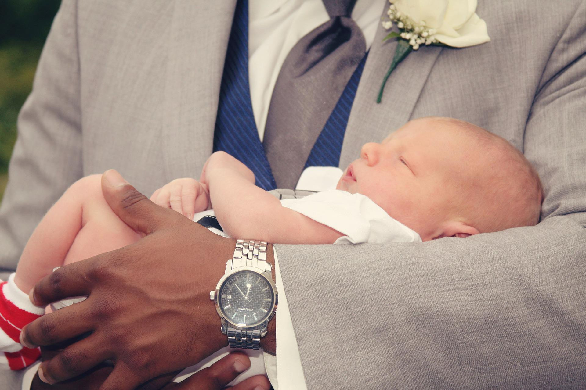 Un nouveau né le jour de son baptème dans les bras de son parrain. 