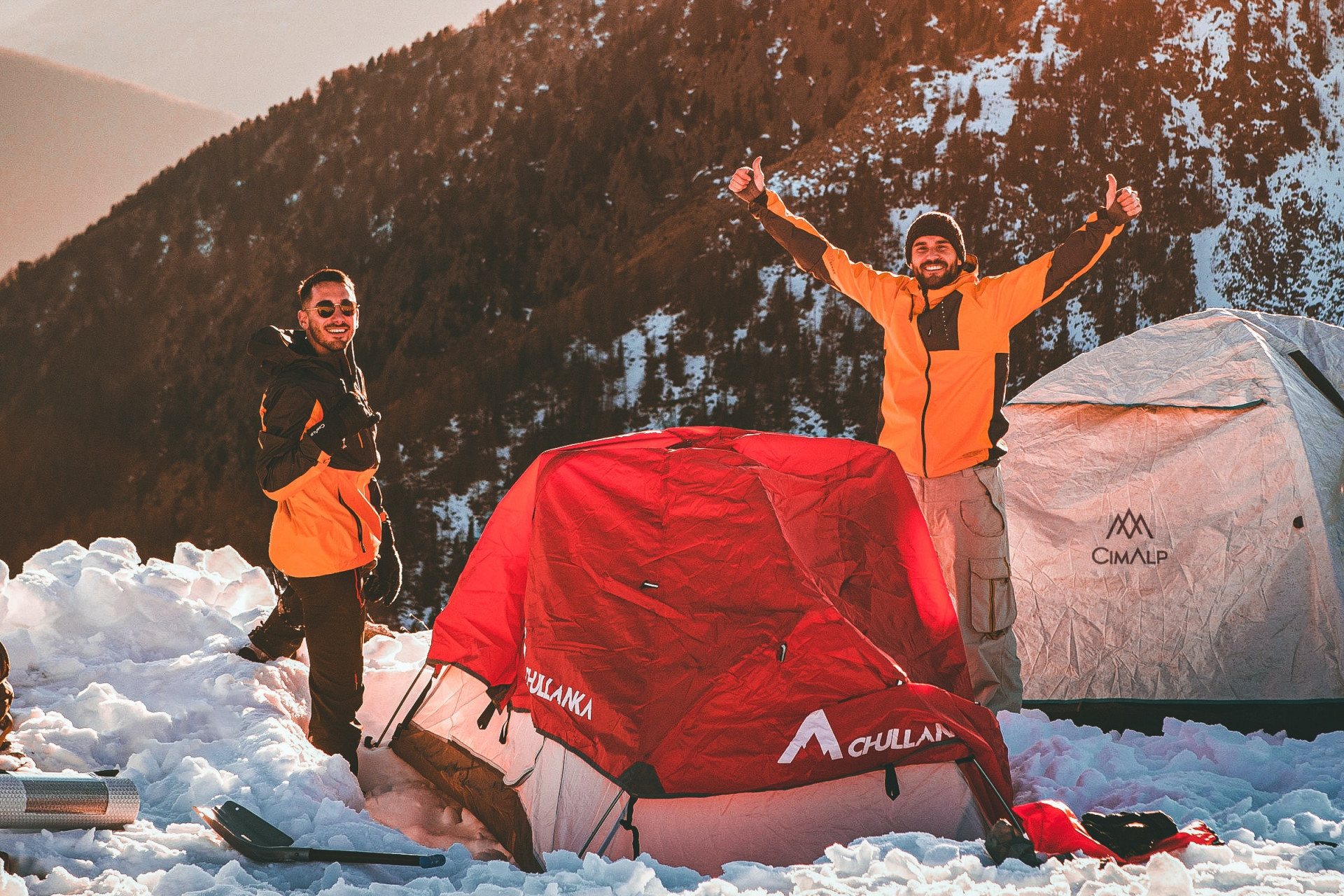 Deux hommes au sommet campent sur une montagne enneigée.