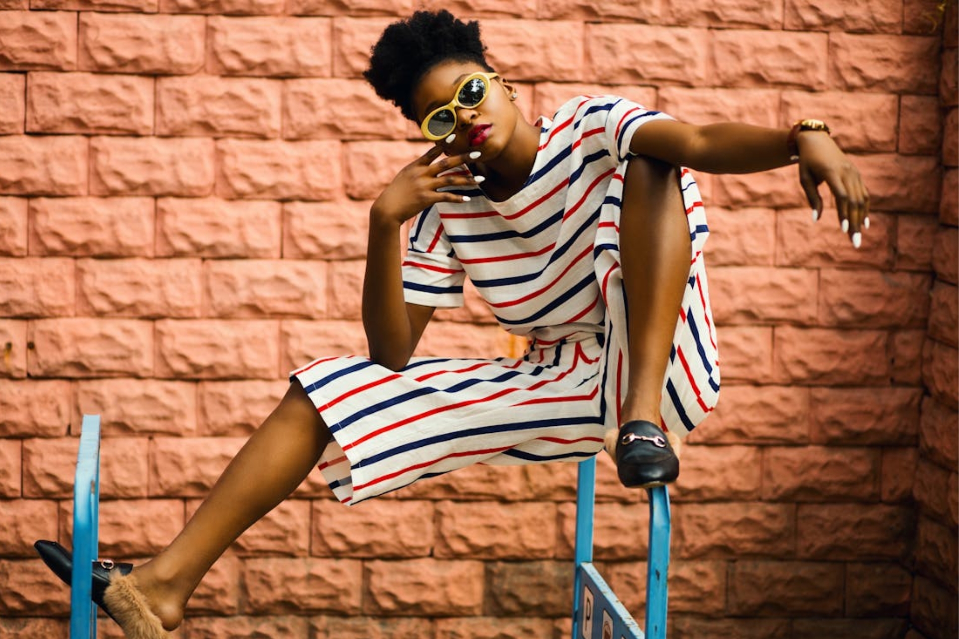 Femme avec un look stylé rayé qui porte des lunettes étroites, arrondies, jaunes.