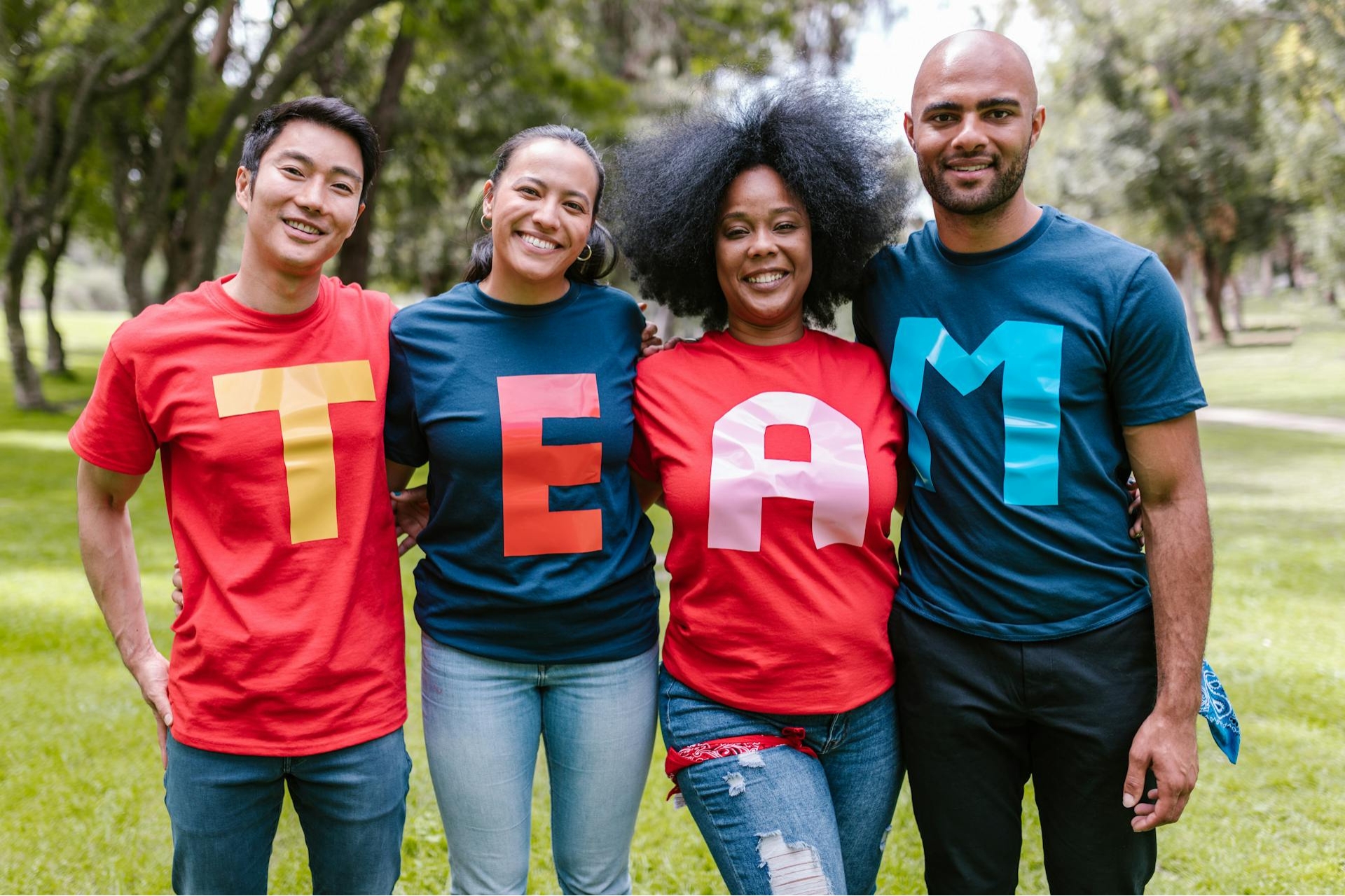 Un groupe de quatre personnes souriantes portant des t-shirts formant le mot 